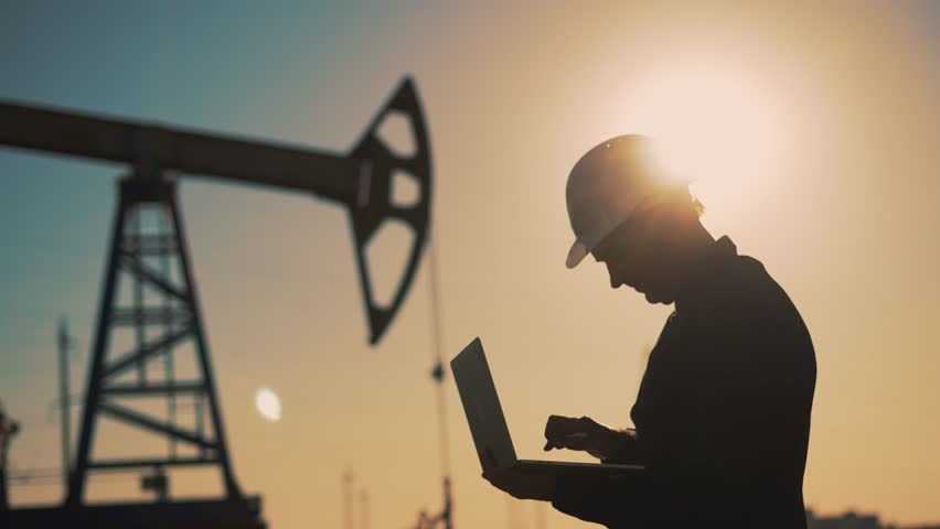 Working engineer.pump silhouette at sunset. An engineer works with tablet at an oil pump. extraction of crude oil. Silhouette of male engineer with tablet working on extraction of crude oil at sunset. - Powered by Shutterstock - Get 15% off with code: PIKWIZARD15
