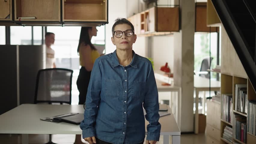 Portrait happy mature bussinesswoman in eyeglasses at modern office. Business leader looking sitting at table and looking at camera.

