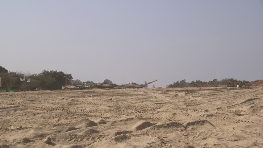A handheld clip of some distant tanks and APCs, waiting for action on the desert soil, lifting some dust by the light wind. few Israeli flags are visible. Be