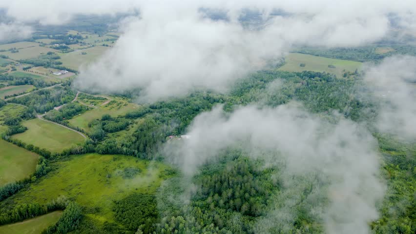 Aerial of low clouds above forests and small farms in rural Minnesota.
