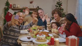 Multi-ethnic family using mobile phone video call online to relative. Attractive diverse group of people having dinner eating food to celebrate holiday Thanksgiving, X-mas eve on dining table at home.
