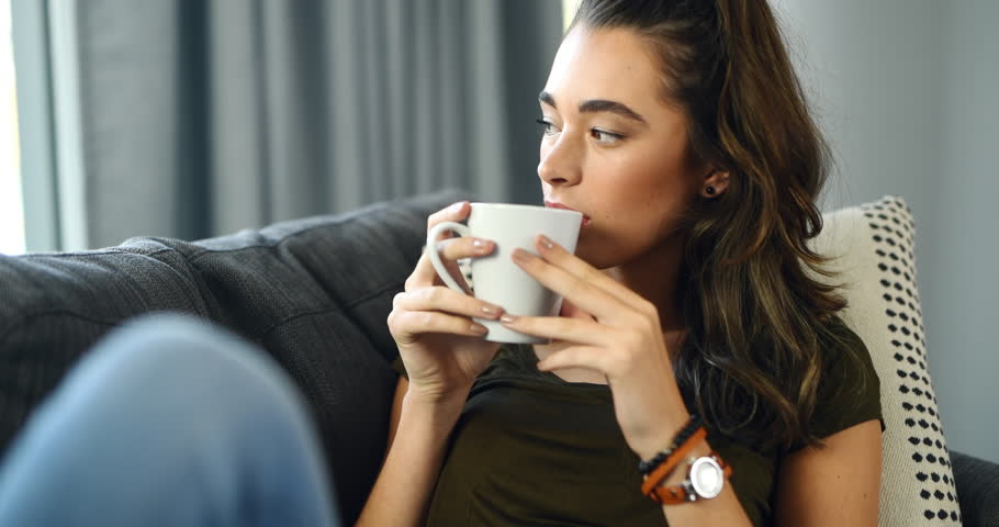 Woman, sofa and thinking with coffee, home and relax with happy memory, vision and peace in living room. Girl, tea cup and smile on lounge couch with ideas, remember or choice with drink in apartment Royalty-Free Stock Footage #1111434243