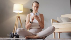 Yoga and meditation online. Healthy lifestyle indoors. Sporty athletic woman wearing beige sportswear and headphones listening to music doing exercises at home gym.