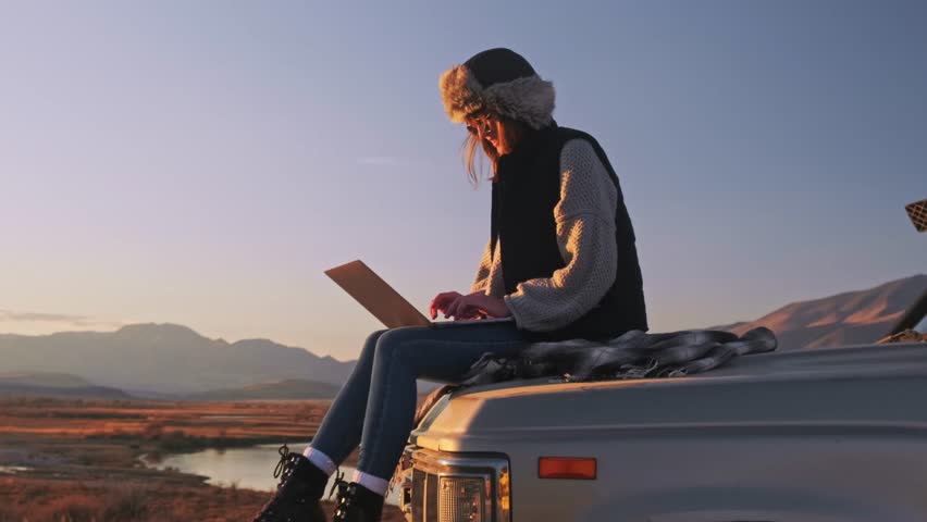 Young Girl hiker sits on trunk a car, uses a laptop, works. Remote freelance work in the mountains. The concept of remote learning, freelancing and modern technology. Outdoor adventure lifestyle. Royalty-Free Stock Footage #1111436721
