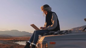 Young Girl hiker sits on trunk a car, uses a laptop, works. Remote freelance work in the mountains. The concept of remote learning, freelancing and modern technology. Outdoor adventure lifestyle. - Powered by Shutterstock - Get 15% off with code: PIKWIZARD15