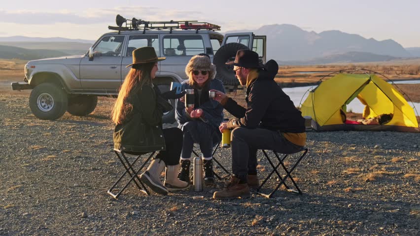 Group of Friends reparing coffee near travel suv. People enjoying a day camping. Autumn vacations and relationship concept. Picnic near car on sunset outside. Domestic travel concept.