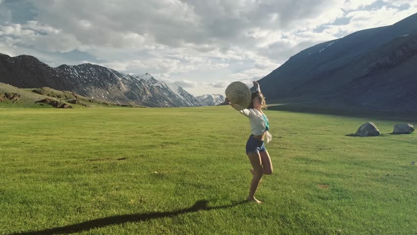 Happy young girl is skipping across the field. Mountains and sky are in the background. Cheerful young woman running with hands stretched wide, feeling happy being in connection with nature. Copy | Shutterstock HD Video #1111440067