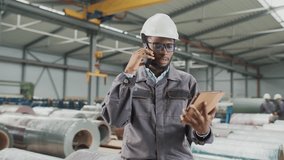 Busy African American worker accepting order from client for manufacture of industrial goods. Serious man talking on phone while entering customer data into tablet. Working with technology in plant. - Powered by Shutterstock - Get 15% off with code: PIKWIZARD15