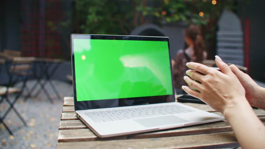 Camera view of laptop with chroma key located on table outdoors. Woman holding cup of hot coffee or tea while sitting on terrace. Looking at green screen while resting in cafe. Concept of technology. | Shutterstock HD Video #1111440391