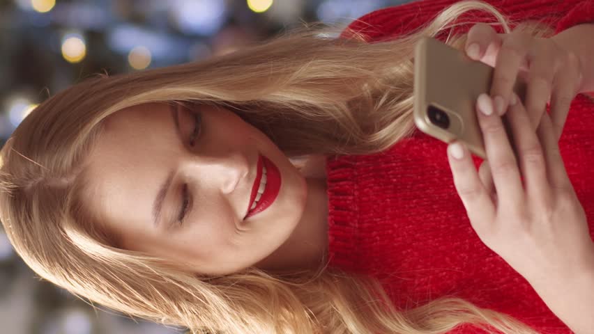 Portrait of blonde Caucasian woman with red lipstick actively messaging with her friends or boyfriend on phone. Young female communicating in social media. Positively smiling while using her gadget. | Shutterstock HD Video #1111440423