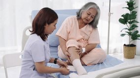 Handheld shot, Elderly Asian patient admitted to hospital A nurse cares for a patient's injured leg bandage. A nurse takes care of patients in a hospital or clinic.