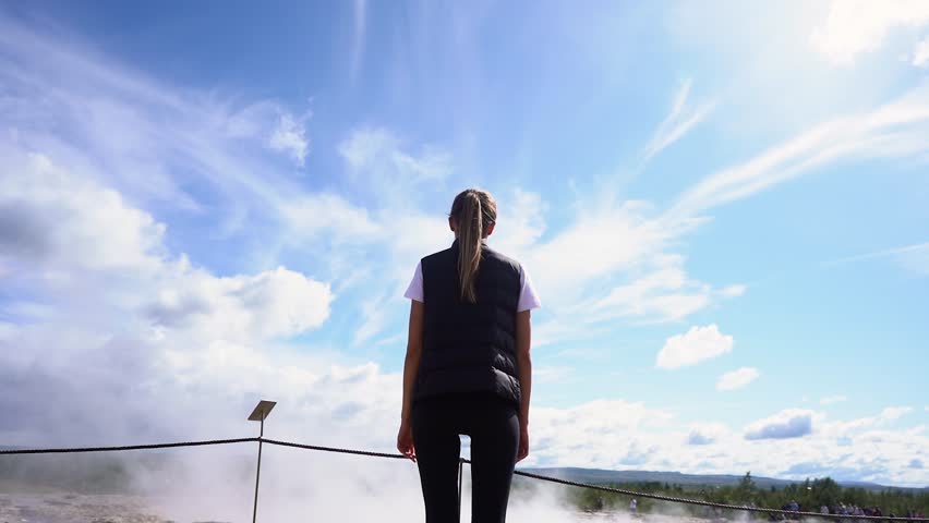 The tourist girl looks at the geyser in Iceland