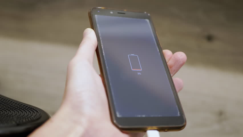Girl is Holding a Smartphone in Hands, which Shows Low Battery Charge on Screen. Close up. Mobile phone low battery indicator in percent. Warning signal. Charge. Indoors. Grey background. Icon. | Shutterstock HD Video #1111449399