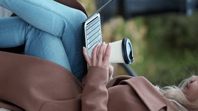 Vertical video. Virtual life. Smiling woman. Digital technology. Positive lady sitting bench in park alley typing laptop holding cup of coffee.