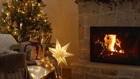 Atmospheric christmas eve at fireplace. Stylish christmas tree with golden lights, wrapped gift, illuminated star and cozy burning fireplace. Winter hygge footage 
