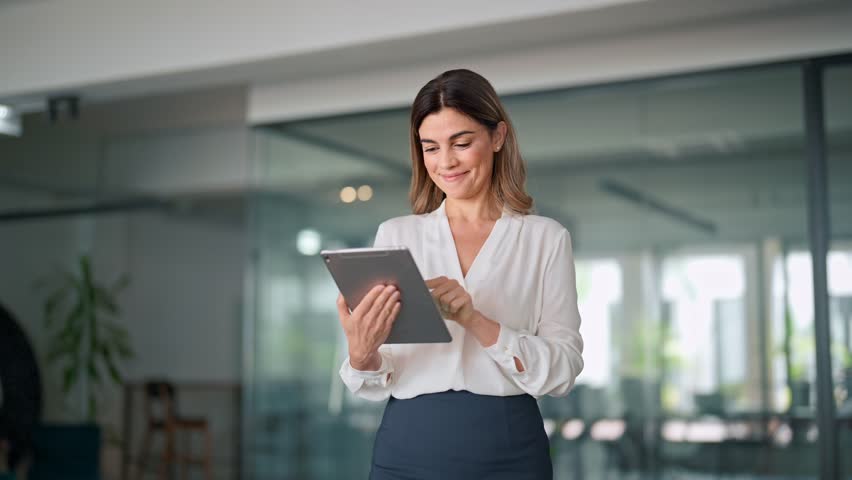 Mid aged busy businesswoman using digital tablet working in office. Middle aged professional business woman company manager standing in office working on corporate tab tech device. Royalty-Free Stock Footage #1111454499