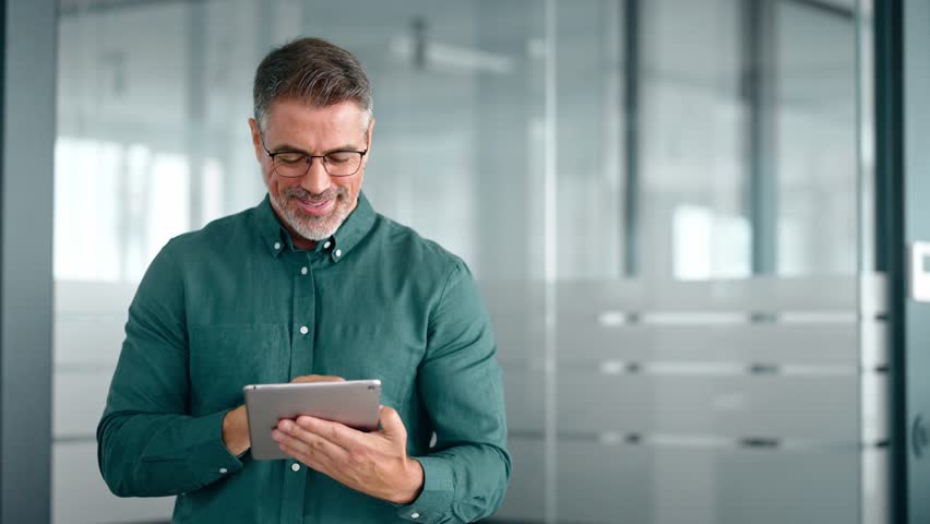 Smiling busy middle aged business man investor using tablet computer, mature older businessman executive manager looking at tab satisfied with finance trading market standing in office. Royalty-Free Stock Footage #1111454525