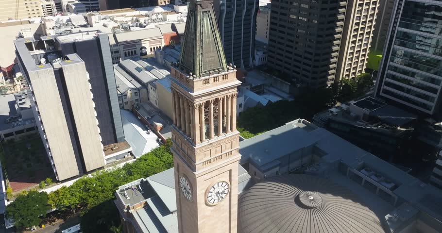 Aerial pullback above Brisbane City Hall clock tower at midday, shadows from skyscrapers