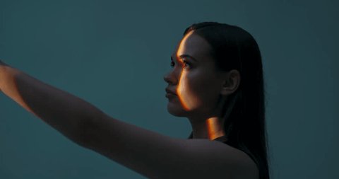 Young female in profile standing in studio isolated in bright light looking up playing with light dansinc with hands. Multicolour future of advertisement concept futuristic time. – Video có sẵn