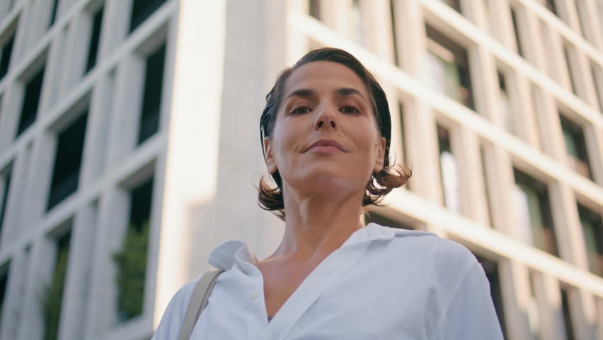 Portrait confident woman posing at business building facade. Smiling lady leader looking camera at downtown district closeup. Proud mature businesswoman contemplating views enjoying summer wind