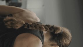 Vertical video. Strong and independent young woman lifts a heavy dumbbell overhead with one hand. Strength training in the gym.