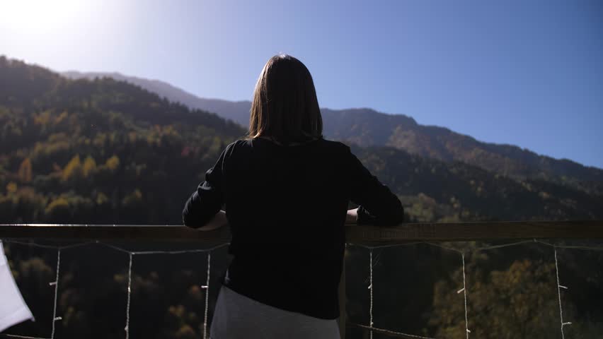 The girl is standing on the balcony against the background of beautiful mountains and the flag of Georgia enjoying the nature