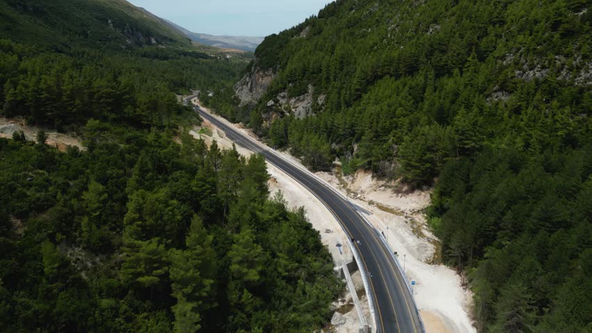 Cars traveling through small mountain road with forest and trees beside the road