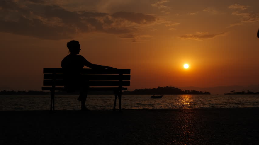 Emotional woman silhouette on city beach. A woman traveler in loneliness pass her free time on the bench on city shore during evening time. Royalty-Free Stock Footage #1111475563