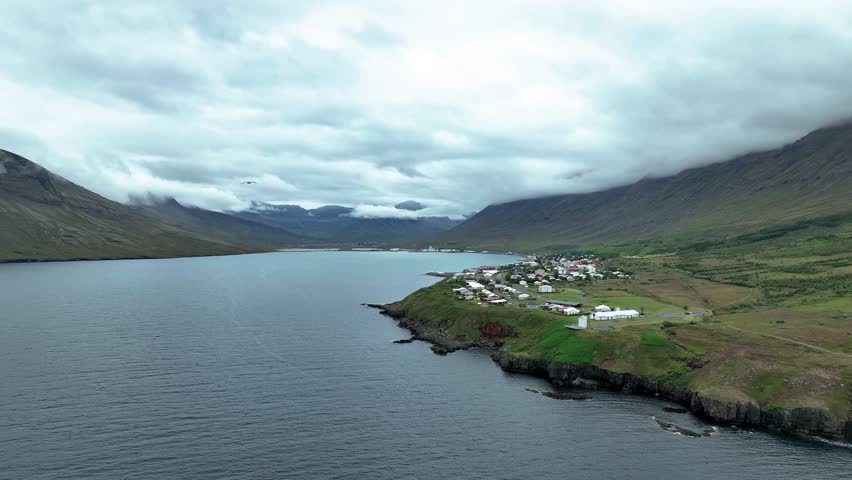 Calm Waters of Fjord Nordfjordur With Neskaupstadur Town By The Mountain In East Iceland. - aerial shot