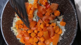 Saute chopped onions and carrots in vegetable oil in a frying pan, turning them with a spatula. The onions are being fried, stirring occasionally. Vertical video