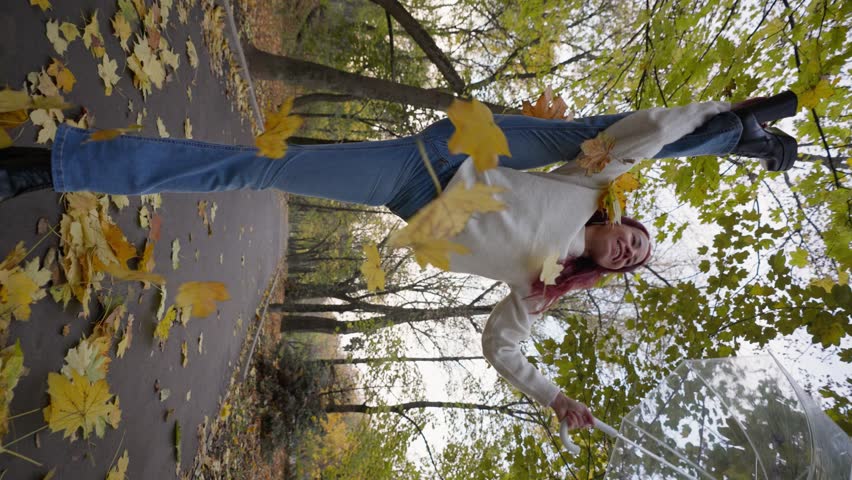 Happy Woman in Jeans and a White Sweater Stands in a Split on one Leg and Raises an Umbrella from Which Autumn Leaves are Flying. Slow Motion, Vertical Video. | Shutterstock HD Video #1111488889