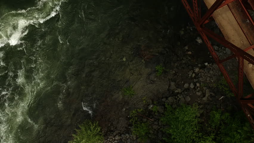 Ariel drone shot of raging river crossing under red steel bridge