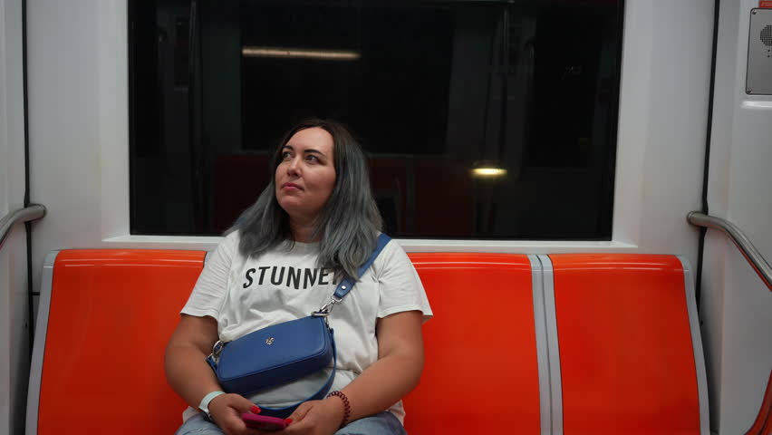 Portrait of pensive plus-size woman sitting in subway train, using public transport, looking around. Front view of thoughtful Caucasian female riding public transport. Shooting in slow motion. | Shutterstock HD Video #1111490999
