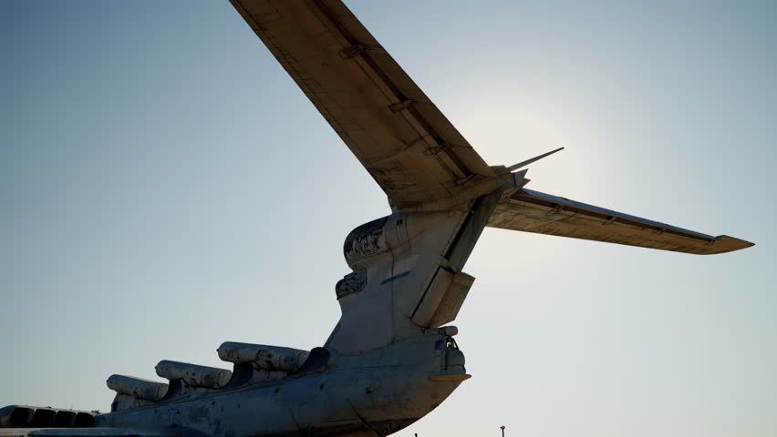 slow-motion shooting of the back of the aircraft in white against a background of blue sky and bright sun, smooth movement of the camera, details of an abandoned ekranoplan, the general plan