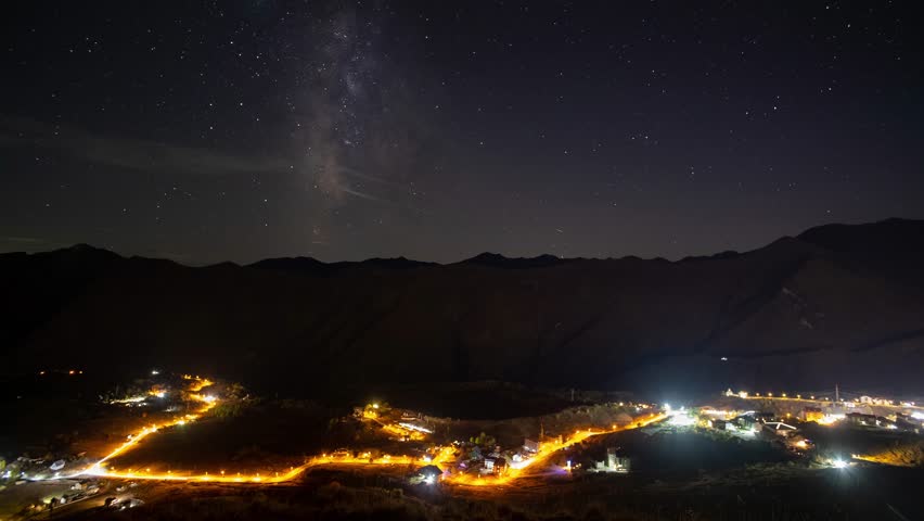 Milky Way and starry sky over a mountain valley with a busy highway and lights and trees, 4k, timelapse
