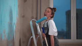 Portrait girl house painter stands smile, looking at camera. Man working, painting wall paint roller with primer or blue paint. Wallpaper for painting. Interior, renovation. Professional occupation. - Powered by Shutterstock - Get 15% off with code: PIKWIZARD15