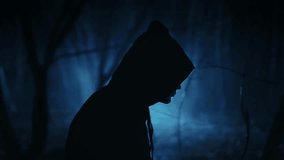 A dark figure in a cloak with a hood in a sinister night forest. Fantasy demon or witcher in the night. - Powered by Shutterstock - Get 15% off with code: PIKWIZARD15