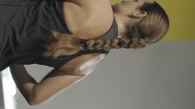 Vertical video. Young Woman on an Elliptical Trainer, Sweaty and Tired, Leaning Forward.