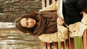 Woman sitting on bench reading in autumn fall park. Young female in coat sitting in city park and reading book. Relaxing outside at weekend. Vertical video