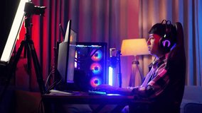 Side View Of Asian Boy Streamer Stretching While Playing Game Over Network On Personal Computer. Live Stream Video Game, Desk Illuminated By Rgb Led Strip Light