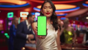 Modern Casino Setting: Gorgeous Asian Brunette Woman Posing with a Mobile Phone with a Green Screen Placeholder Space for Advertising or Commercial Materials for a Gambling Industry - Powered by Shutterstock - Get 15% off with code: PIKWIZARD15
