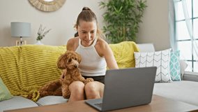 Young caucasian woman with dog doing video call using laptop sitting on the sofa at home