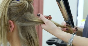 Close-up view of stylist hairdresser making hairstyle using curling tongs