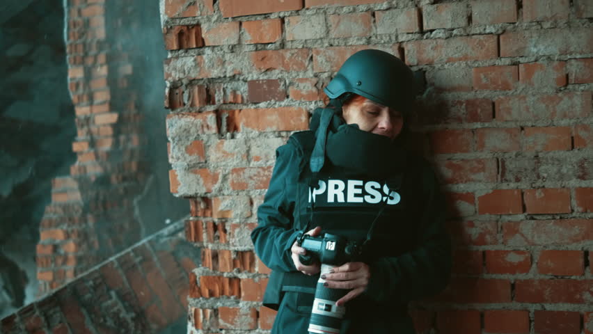 Distraught scared female war journalist taking photos during military operation under fire hiding behind a wall | Shutterstock HD Video #1111521059