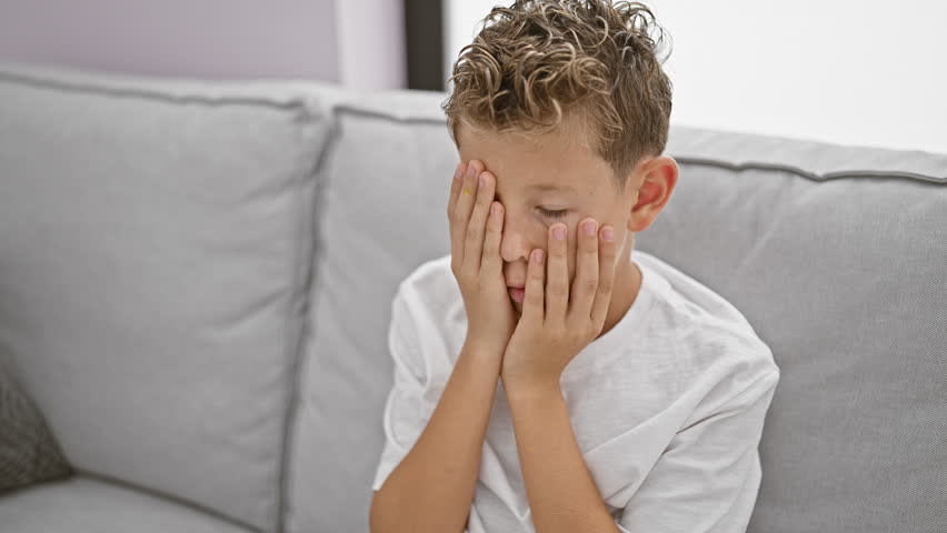 Adorable blond child sitting in despair on sofa at home, plagued by stress and frustration | Shutterstock HD Video #1111521303