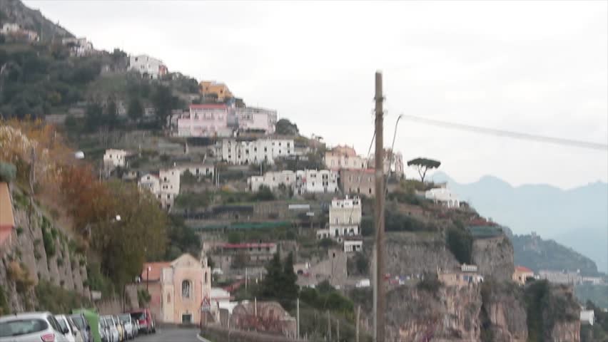 Amalfi coast mountain town village homes houses on cliff mountain shot from moving driving vehicle on road street approaching town village homes buildings with parked cars on side of road | Shutterstock HD Video #1111528845