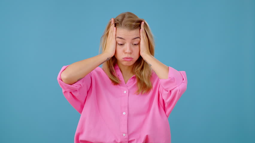 Young woman rubs temples suffering from throbbing headache. Blonde lady with pained expression massages forehead trying to alleviate persistent headache