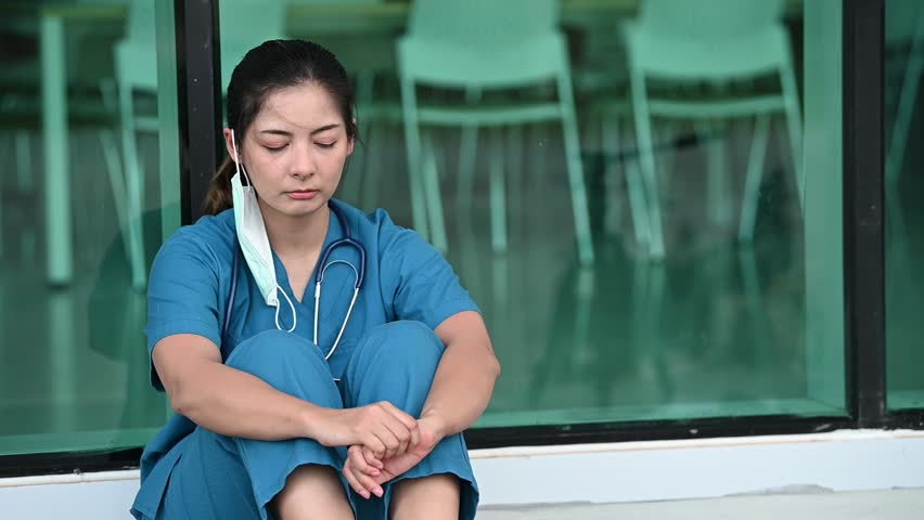 Tired depressed female asian scrub nurse wears face mask blue uniform sits on hospital floor,Young woman doctor stressed from hard work Royalty-Free Stock Footage #1111531887