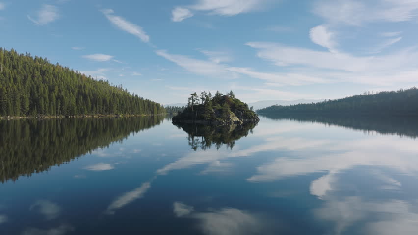 Beautiful nature of Tahoe lake and emerald bay island. Natural landscape of Tahoe lake and mirror like reflection water surface with scenic clouds. Scenic aerial of rocky island in middle of lake 4K