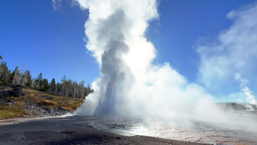 Cinematic Grand geyser Old Faithful sun glare sunrise sunset eruption explosion steam Yellowstone National Park observation deck Upper Geyser Basin fall autumn beautiful blue sky slow motion still